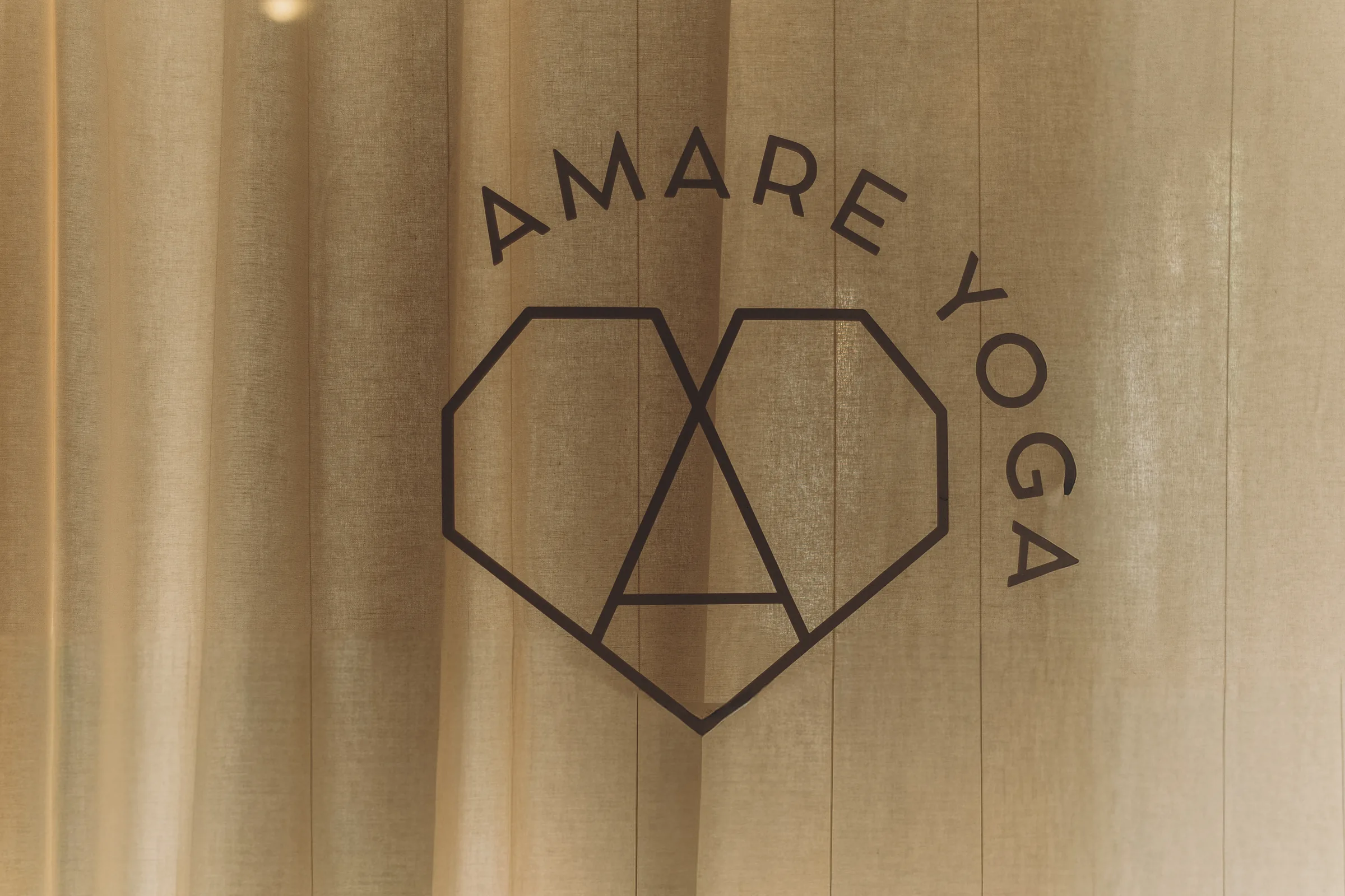 Amare Yoga logo, a heart-shaped line drawing, on a natural linen curtain