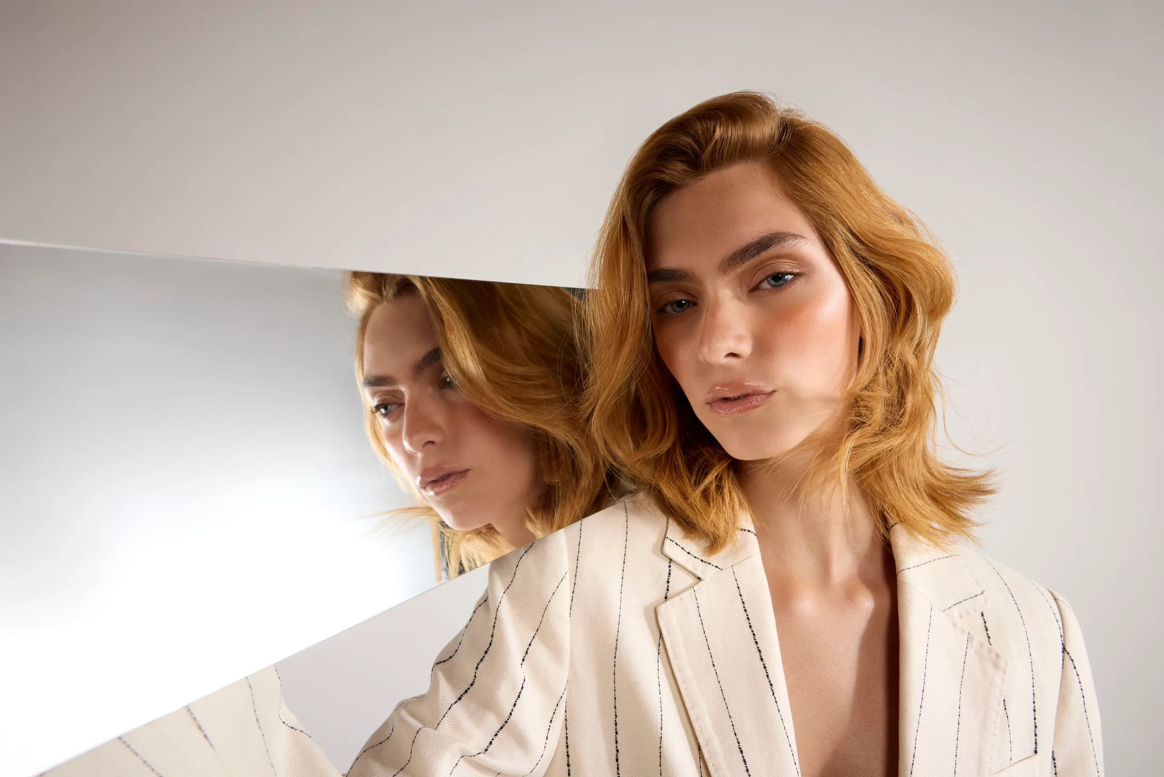 Model with wavy auburn hair and a striped jacket beside a mirror reflecting her profile — Iconic Visions campaign
